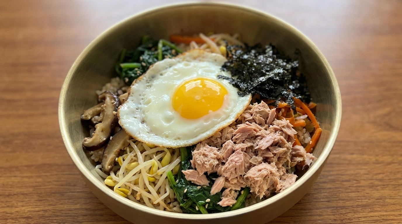 Kolorowa miska tuńczyka bibimbap zawierająca doprawiony ryż, świeże warzywa, grzyby, płatki wodorostów, tuńczyka z puszki oraz jajko sadzone.
