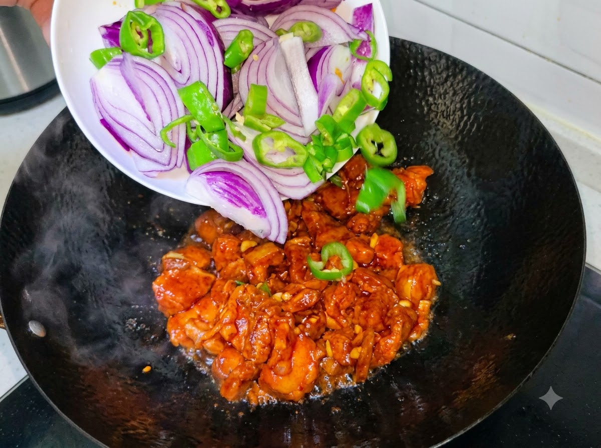 Plastry fioletowej cebuli i zielonych papryczek chili wsypywane z białego talerza do woka ze smażącym się boczkiem wieprzowym.