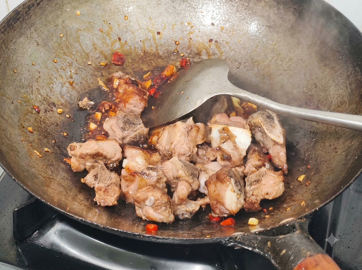 Obsmażone żeberka wieprzowe mieszane w woku z sosem, posiekanymi papryczkami chili i czosnkiem za pomocą metalowej łopatki.