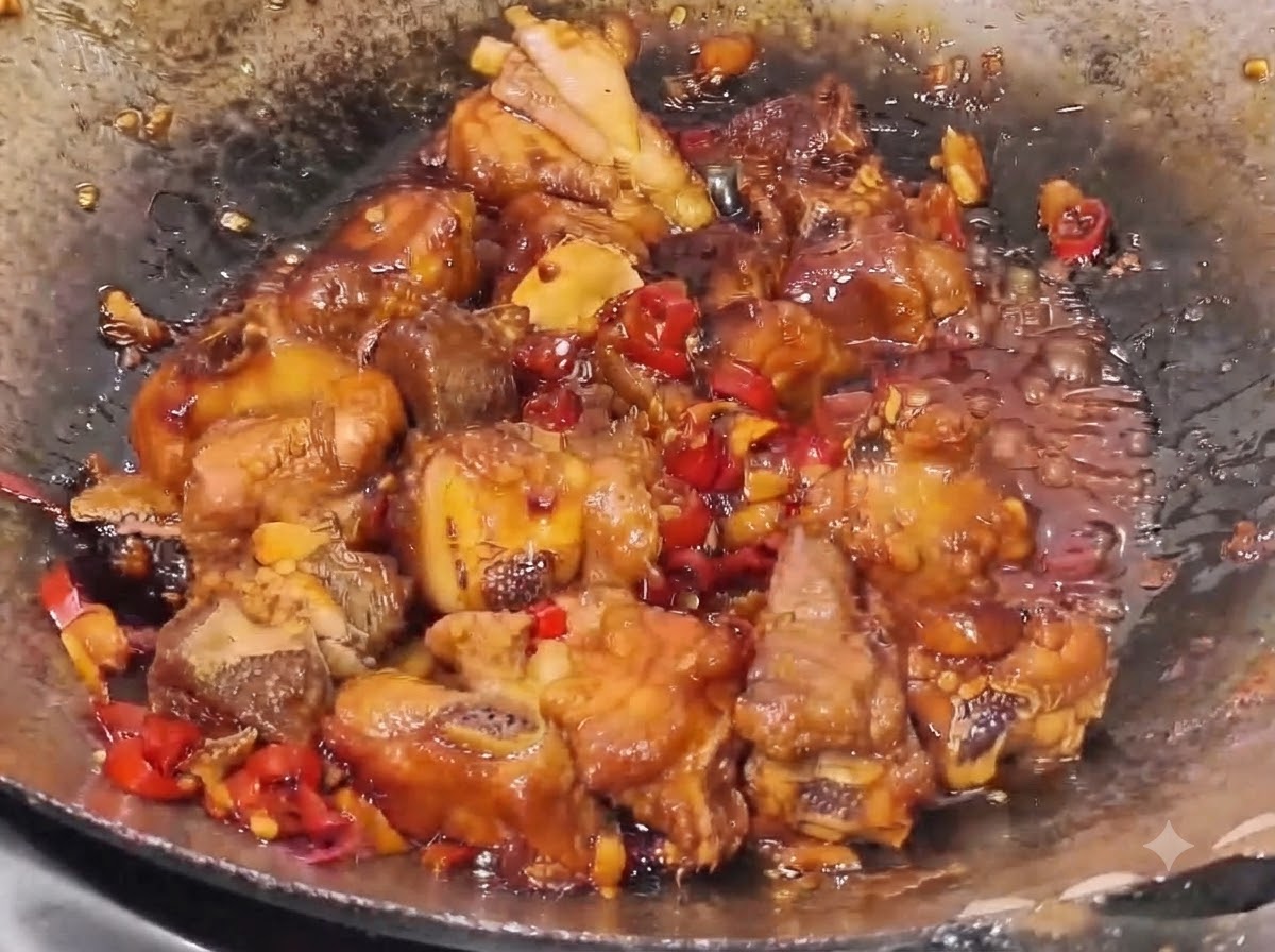 Żeberka wieprzowe duszące się w gęstym, ciemnym sosie z widocznymi kawałkami czerwonego chili i czosnku w woku.
