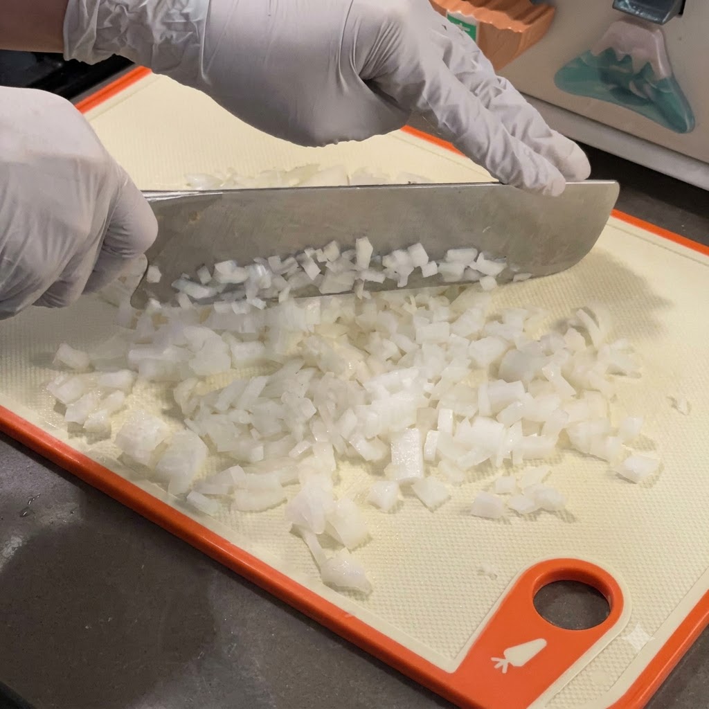 Drobno pokrojona biała cebula podsmażająca się na gorącej patelni żeliwnej.
